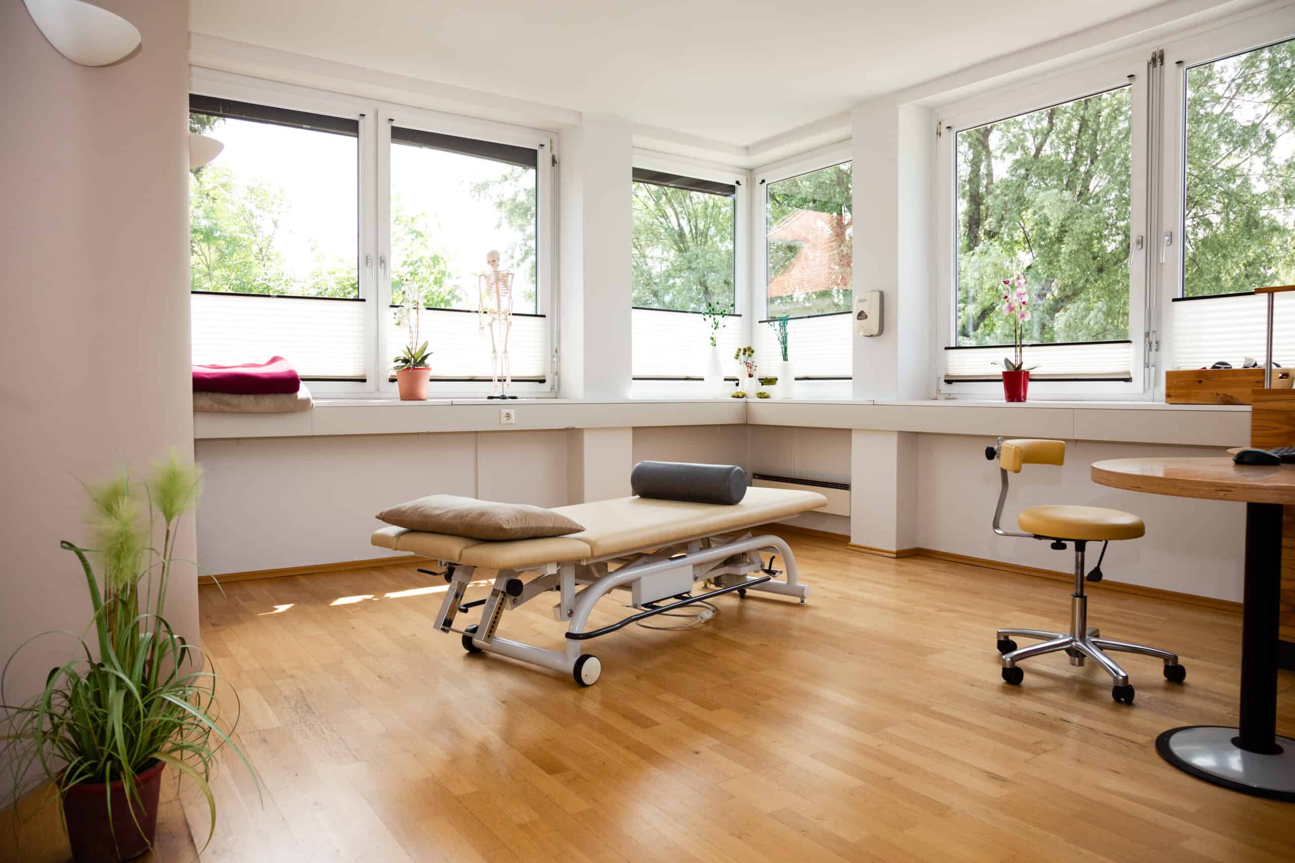 Behandlungsraum mit weitläufigem Holzboden und einer beige-farbenen Behandlungsliege